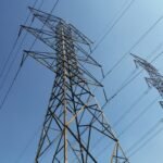 Low angle view of towering electrical transmission lines and pylons under a clear blue sky, conveying energy and electricity concepts.