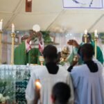 Priest performing Eucharist during a Catholic Mass with ceremonial candles and altar.