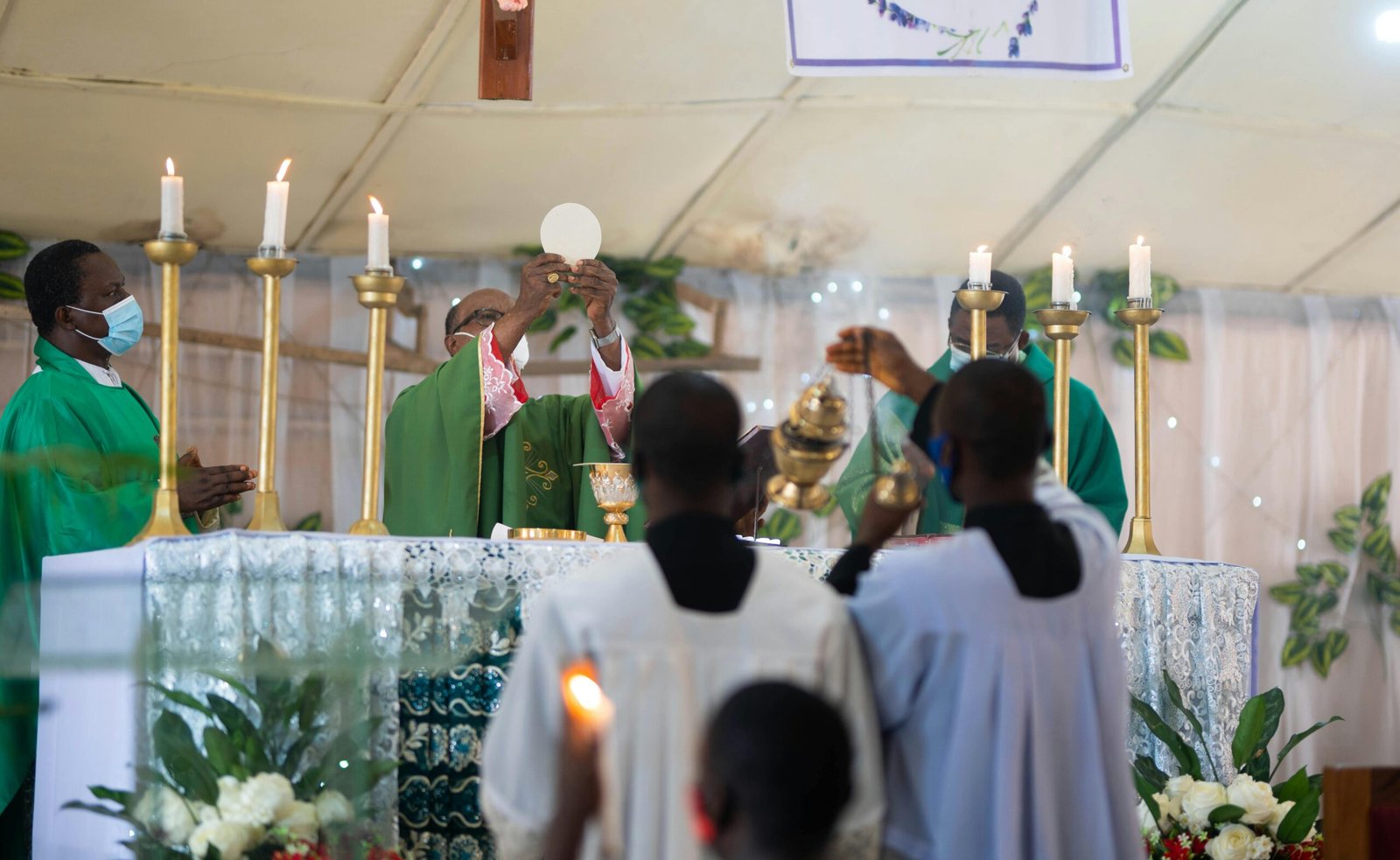 Priest performing Eucharist during a Catholic Mass with ceremonial candles and altar.